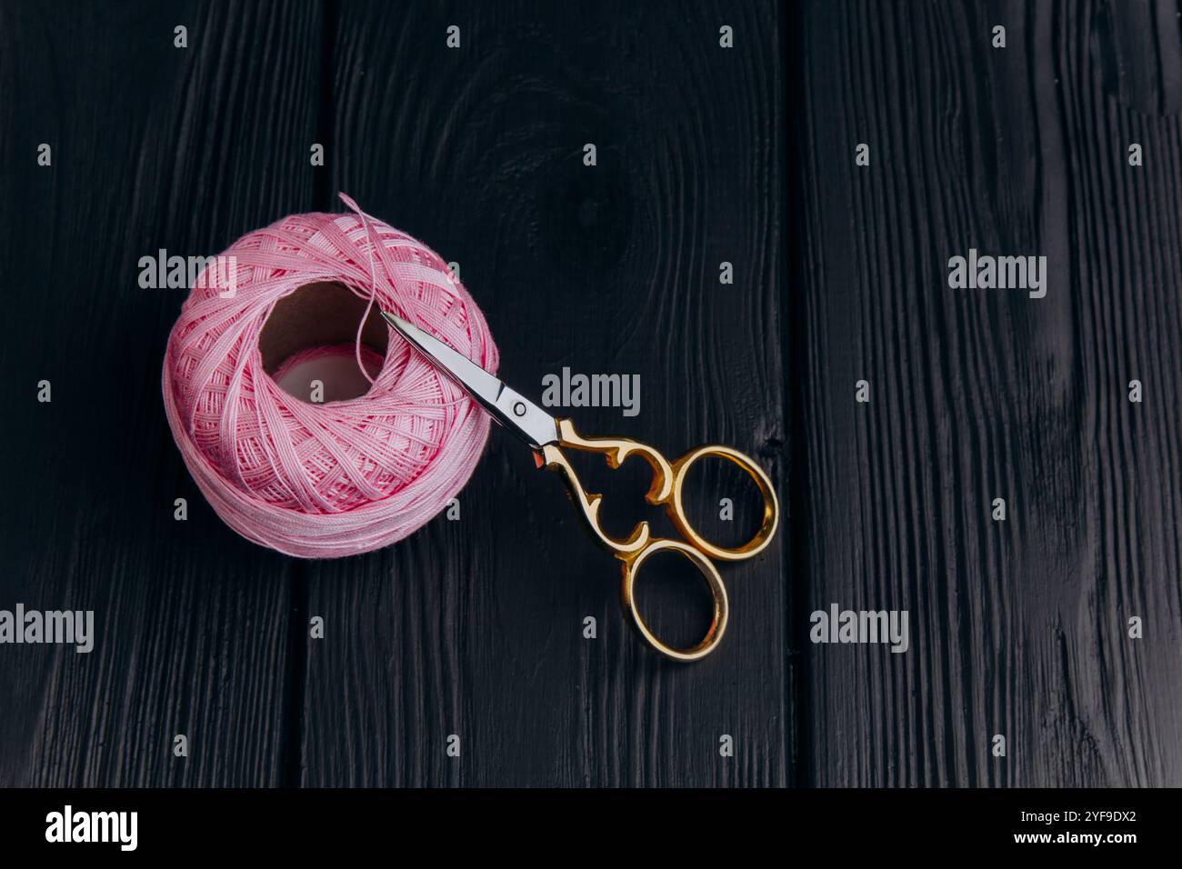 Forbici vintage dorate e uno spiedino rosa pallido di filo di seta per la lavorazione degli aghi giacciono su un tavolo di legno scuro. Minimalismo nella foto. Foto Stock