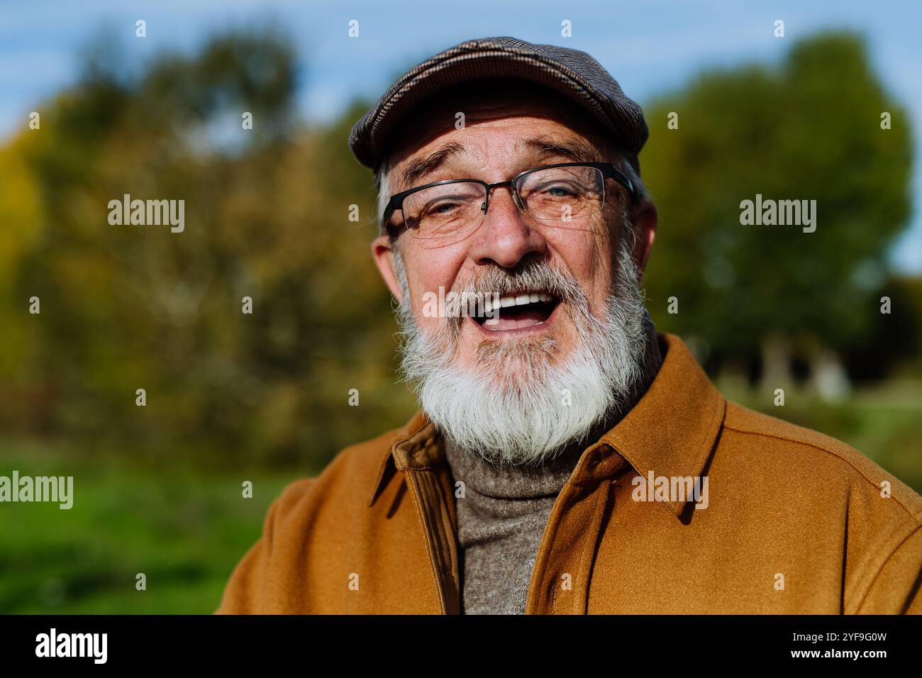 Ritratto di un uomo anziano amico con barba grigia. Senior in piedi all'aperto in mezzo alla natura, guardando la macchina fotografica e sorridendo. Foto Stock