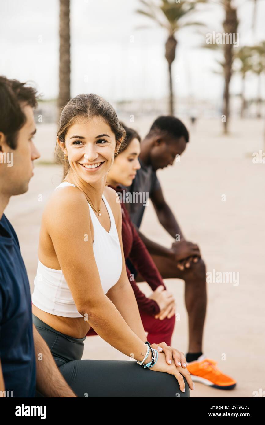 Un gruppo di giovani amici che si godono un momento informale all'aperto. Sono seduti su un sentiero, sorridenti e impegnati in conversazione, circondati da palme. Foto Stock Un gruppo di giovani amici che si godono un momento informale all'aperto. Sono seduti su un sentiero, sorridenti e impegnati in conversazione, circondati da palme. Foto Stock
