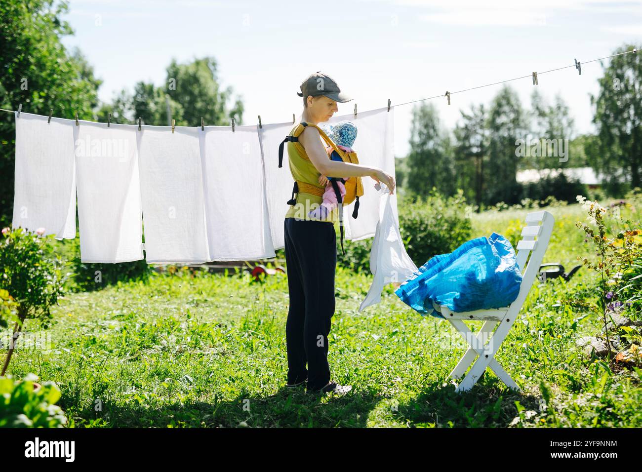 Mamma che porta il bambino mentre appende il bucato sulla clothesline Foto Stock