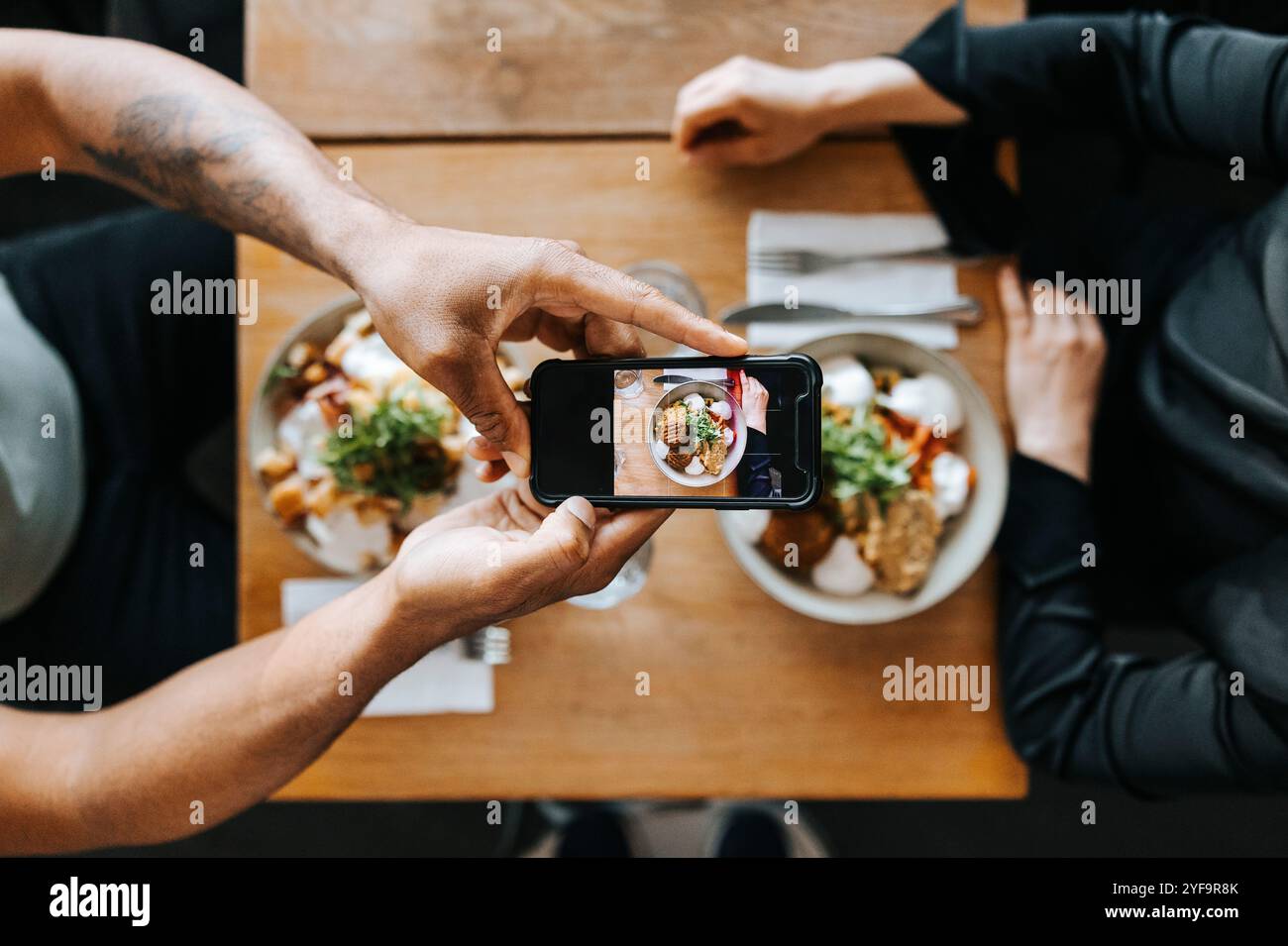 Parte centrale della coppia che fotografa il cibo con un cellulare nel ristorante Foto Stock