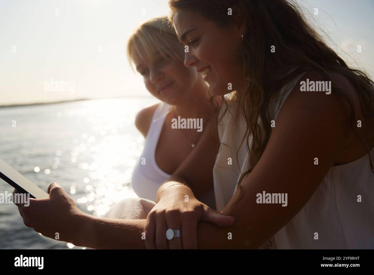 Sorridendo amiche che usano il telefono a Lakeshore Foto Stock