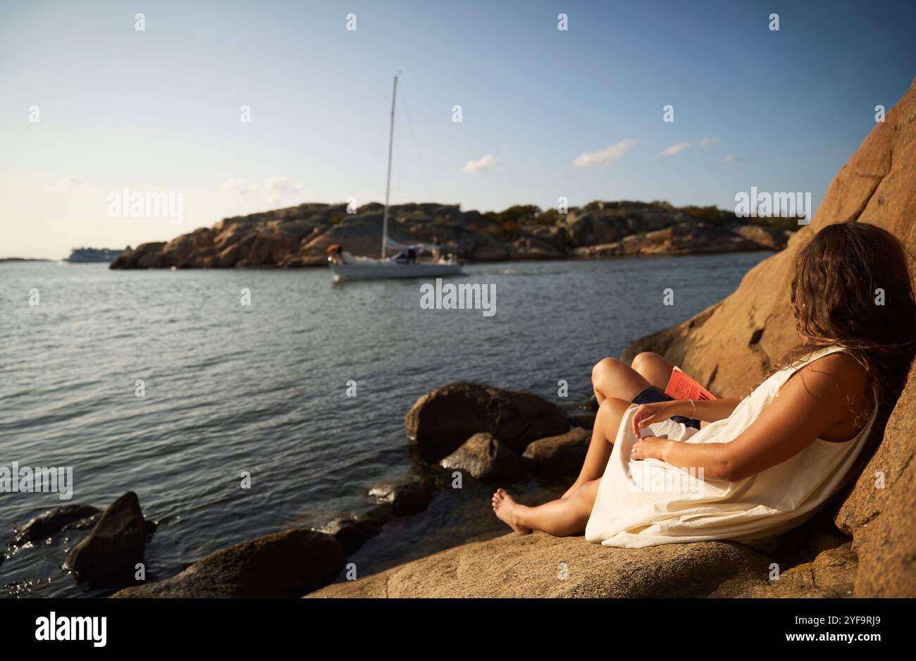 Vista laterale di una giovane donna seduta con un'amica sulla riva del lago Foto Stock