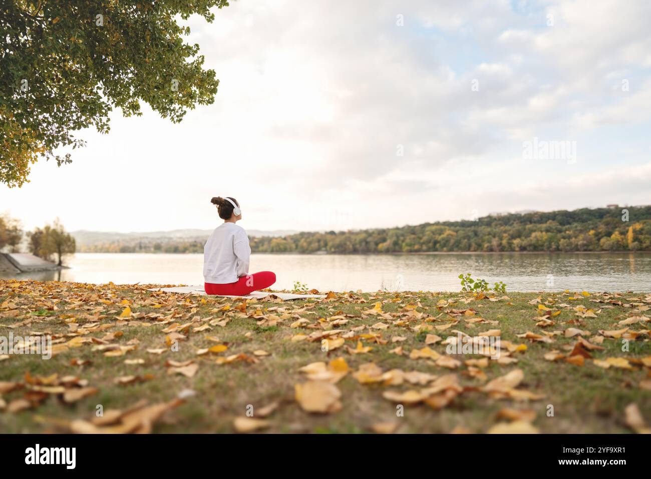 Donna serena che pratica la meditazione in riva al fiume, abbracciando la natura e il benessere. Scarico della sollecitazione. Foto Stock