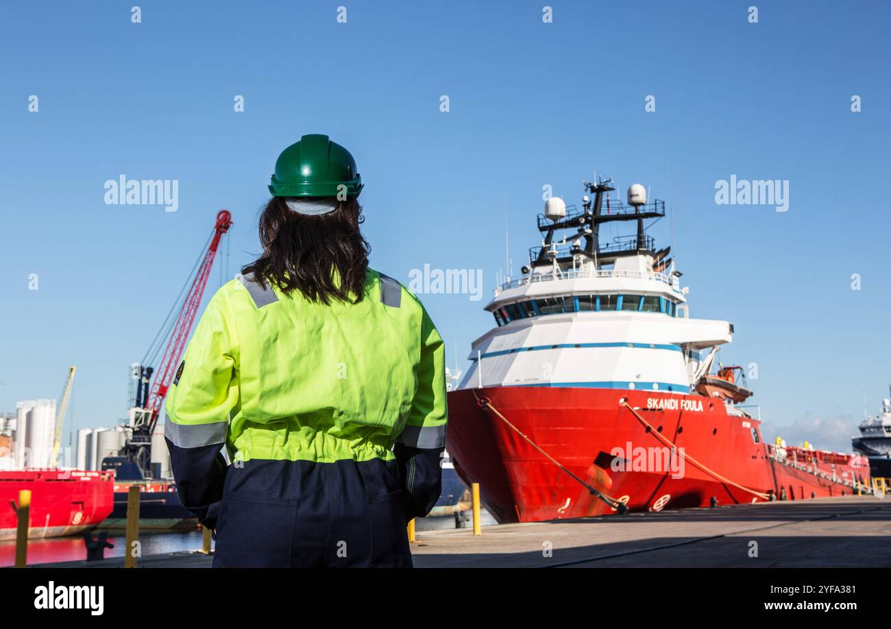 Lavoratore di Feamle in dpi accanto alle navi di rifornimento di petrolio in un porto Foto Stock