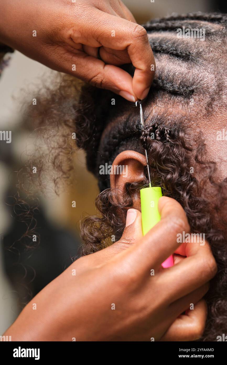 Parrucchiere che fa trecce all'uncinetto sul cliente con capelli afro Foto Stock