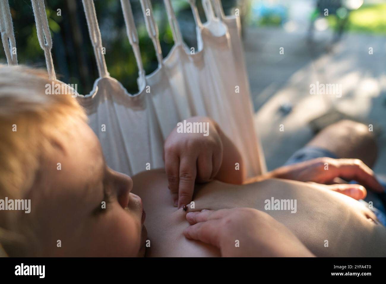 Un bambino di 3 anni guarda un insetto sul petto mentre è sdraiato su un'amaca. Foto Stock