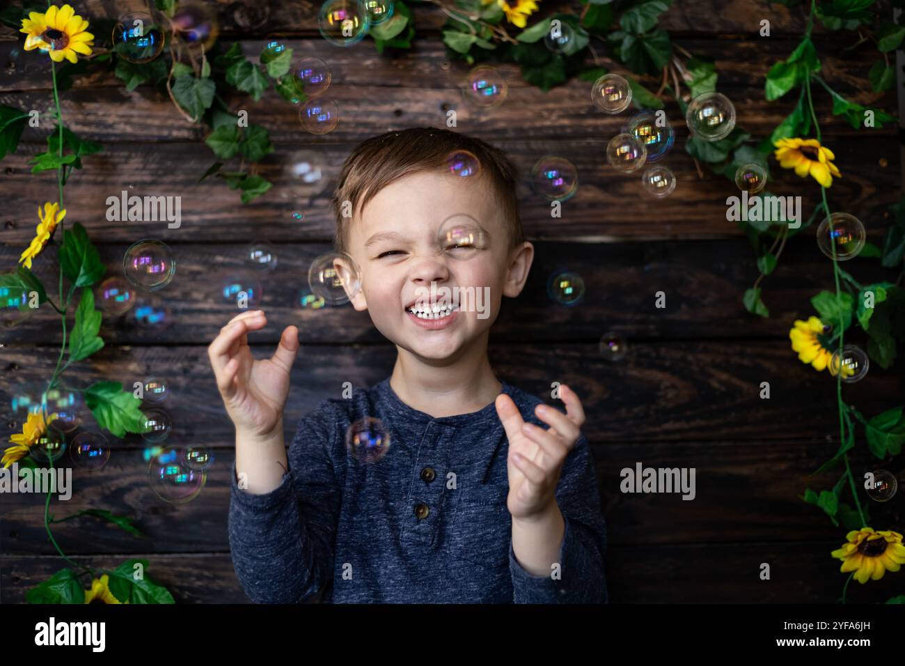 Bambino sorridente che gioca con le bolle su uno sfondo floreale in legno Foto Stock