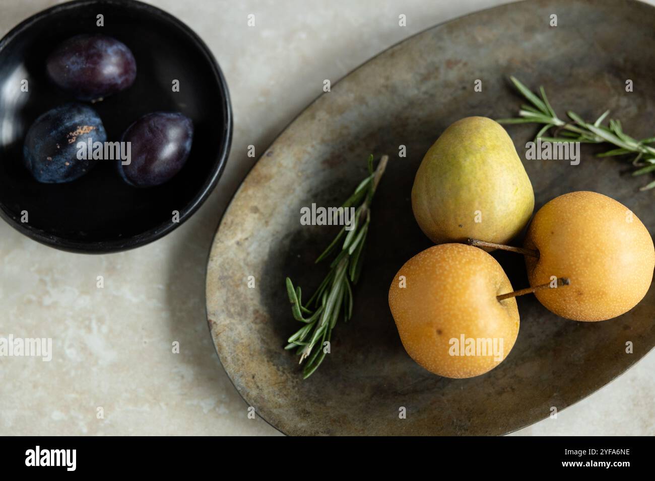 Disposizione minimalista di pere, prugne e rosmarino su un vassoio rustico Foto Stock