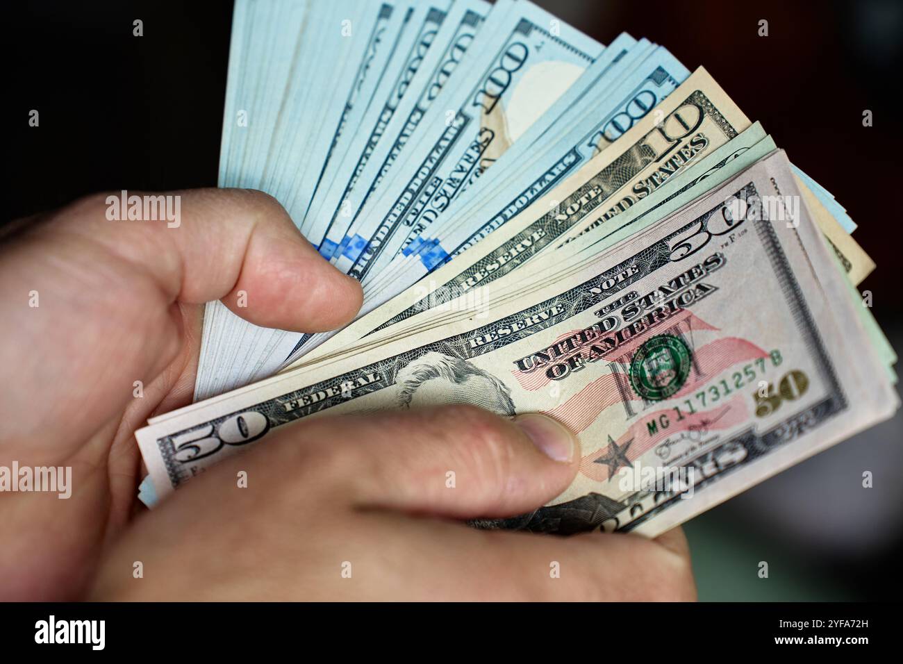 Primo piano di mani che contano una pila di banconote da un dollaro. Uomo che tiene in mano dollari americani in contanti. Concetto di gestione del contante, ricchezza o transazioni finanziarie Foto Stock