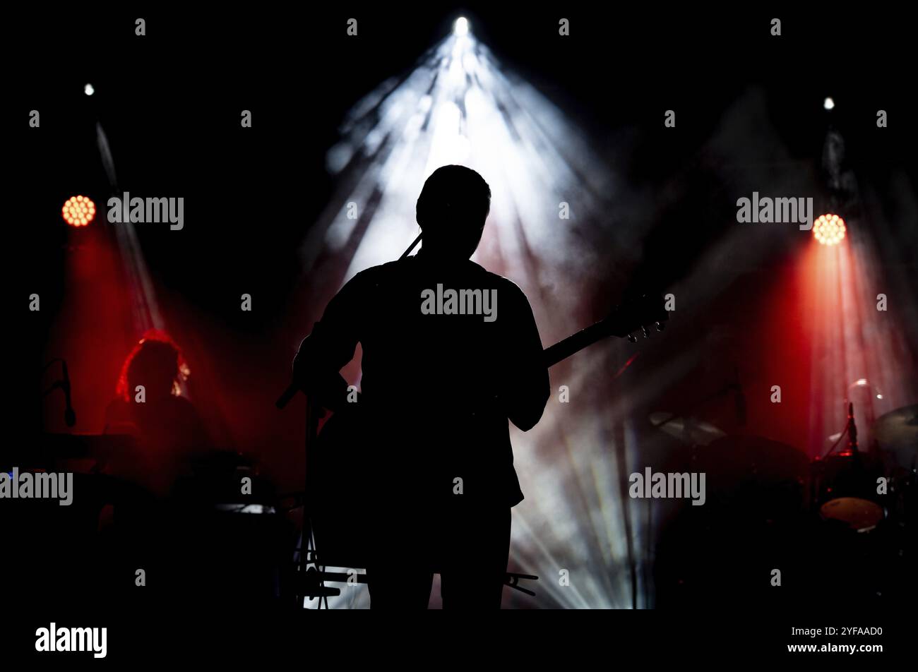 Musicista che suona la chitarra esibendosi sul palco sotto la luce spot. Silhouette di un artista musicale e di una band sul palco Foto Stock