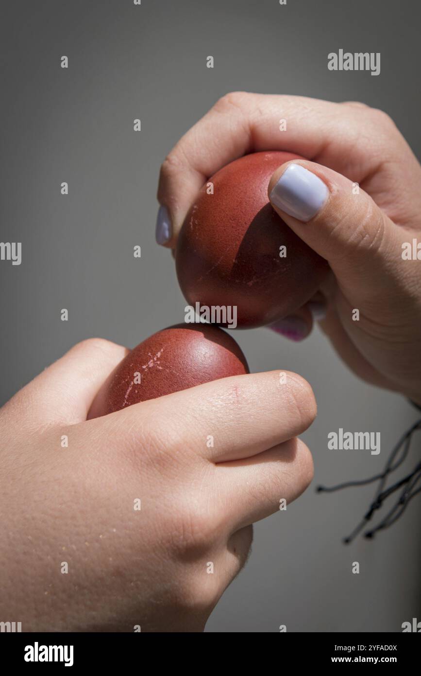 Due mani che tengono le uova di pasqua rosse che cercano di rompere le uova per trovare il vincitore. Tradizionale concorso pasquale Foto Stock