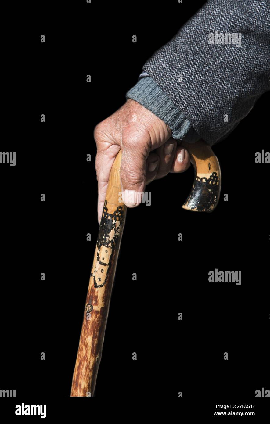 Uomo anziano con un tradizionale bastone da passeggio in legno isolato su sfondo nero. Il bastone viene utilizzato per fornire supporto e aiutarlo a camminare in modo sicuro Foto Stock