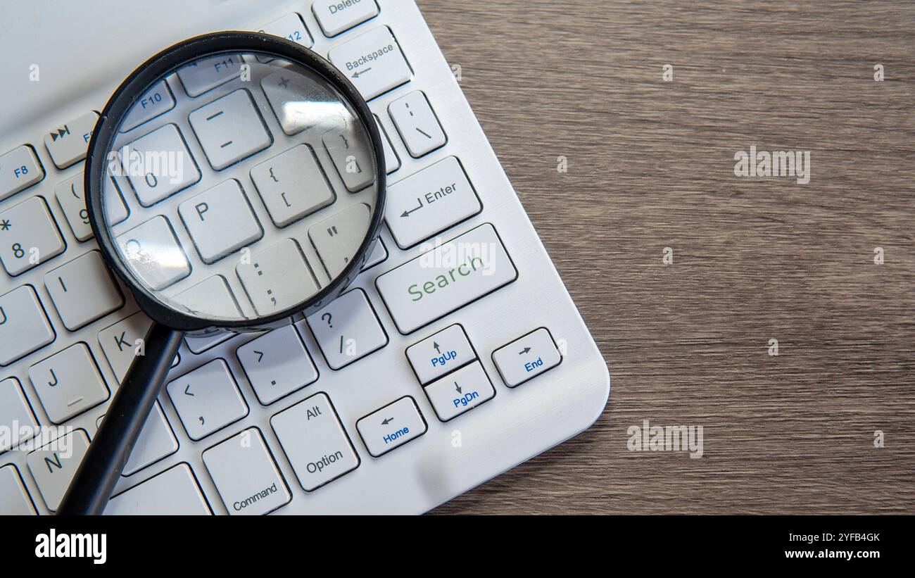 Una lente di ingrandimento è posizionata sulla tastiera di un computer, con l'obiettivo che passa sopra il tasto "Cerca". Ricerca online, indagine, analisi dei dati o t Foto Stock