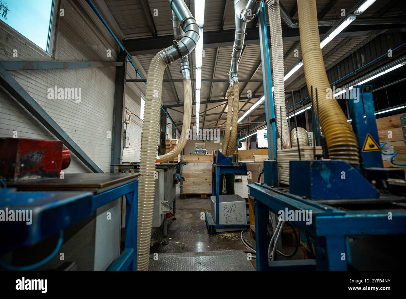 Macchine industriali per la lavorazione del legno con grandi tubi di scarico e sistemi di ventilazione in un ambiente di fabbrica ben illuminato Foto Stock