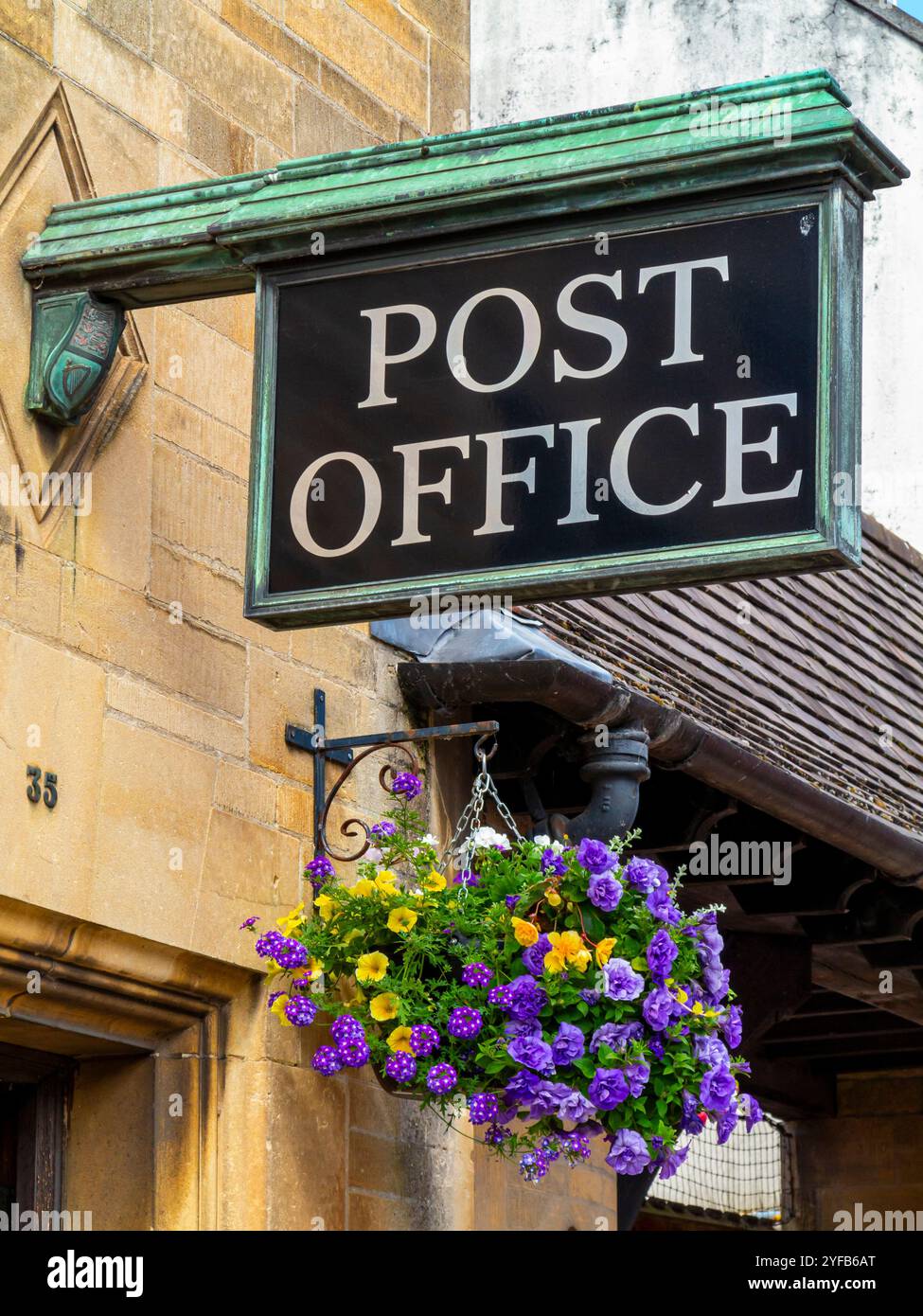 Insegna tradizionale all'esterno di una filiale di un ufficio postale a Glastonbury, Somerset, Inghilterra, Regno Unito, con fiori nel cesto appeso sottostante. Foto Stock