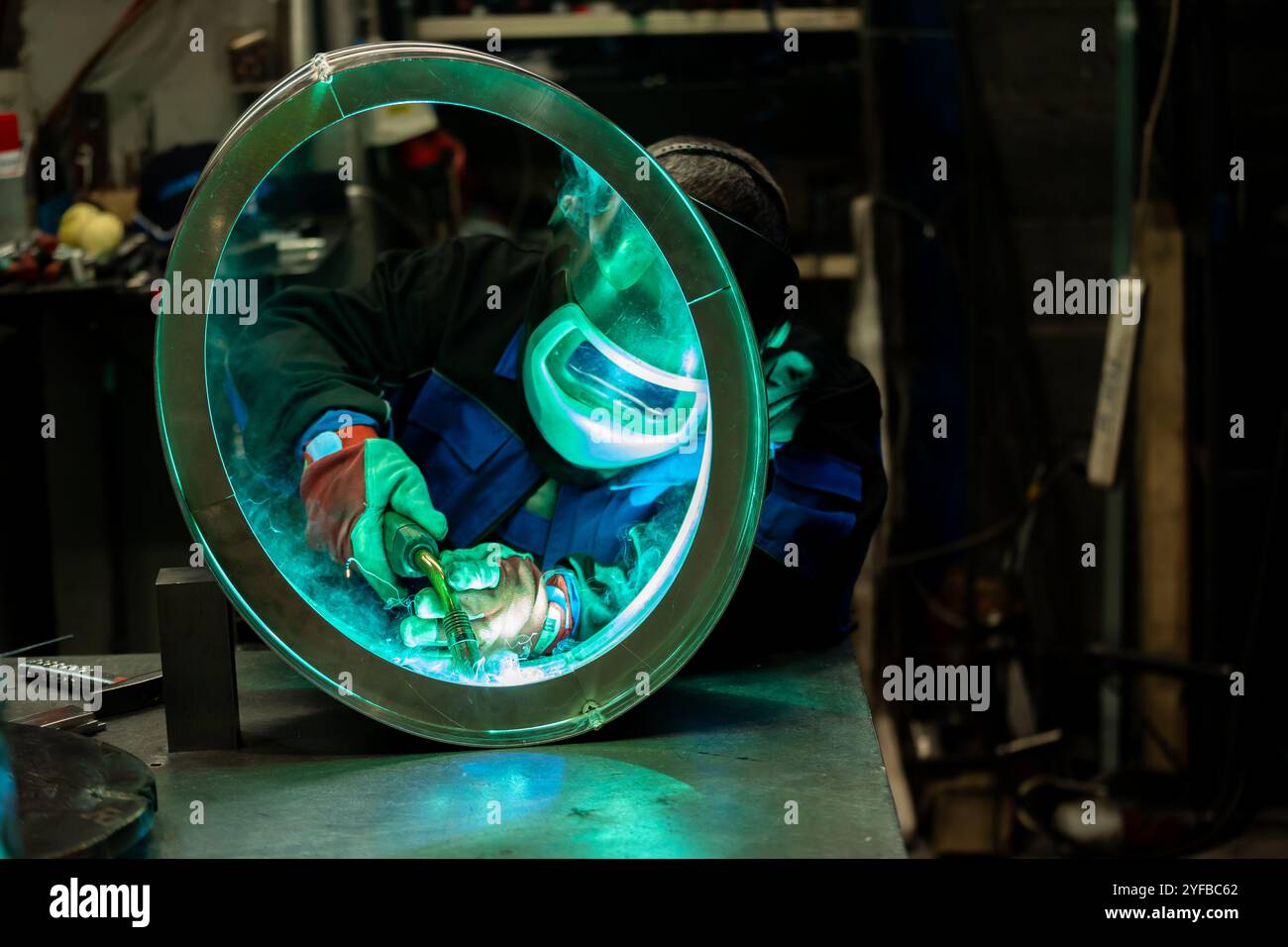 Saldatrice che lavora con competenza su un anello metallico di grandi dimensioni, saldando con cura i giunti in un'officina ben attrezzata. Foto Stock