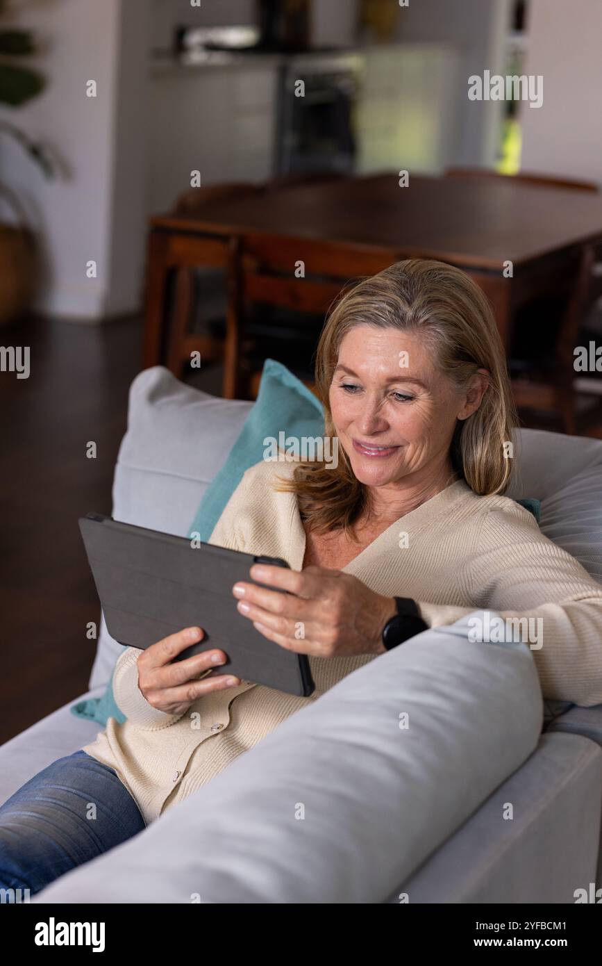donna anziana che si rilassa sul divano usando un tablet a casa, sorridente Foto Stock