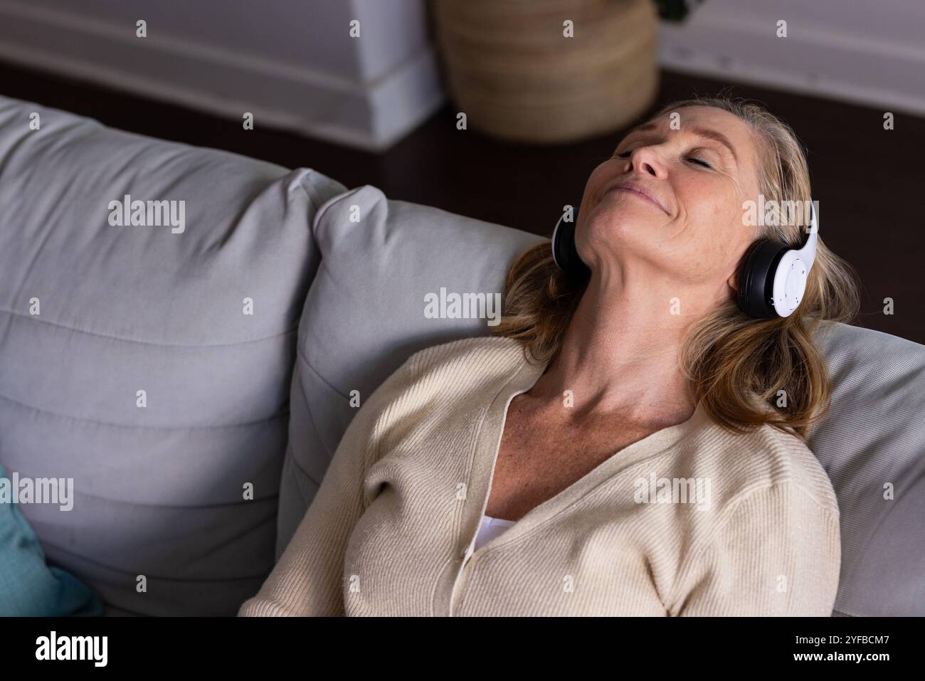 Rilassati sul divano, donna anziana che ascolta musica con le cuffie a casa Foto Stock