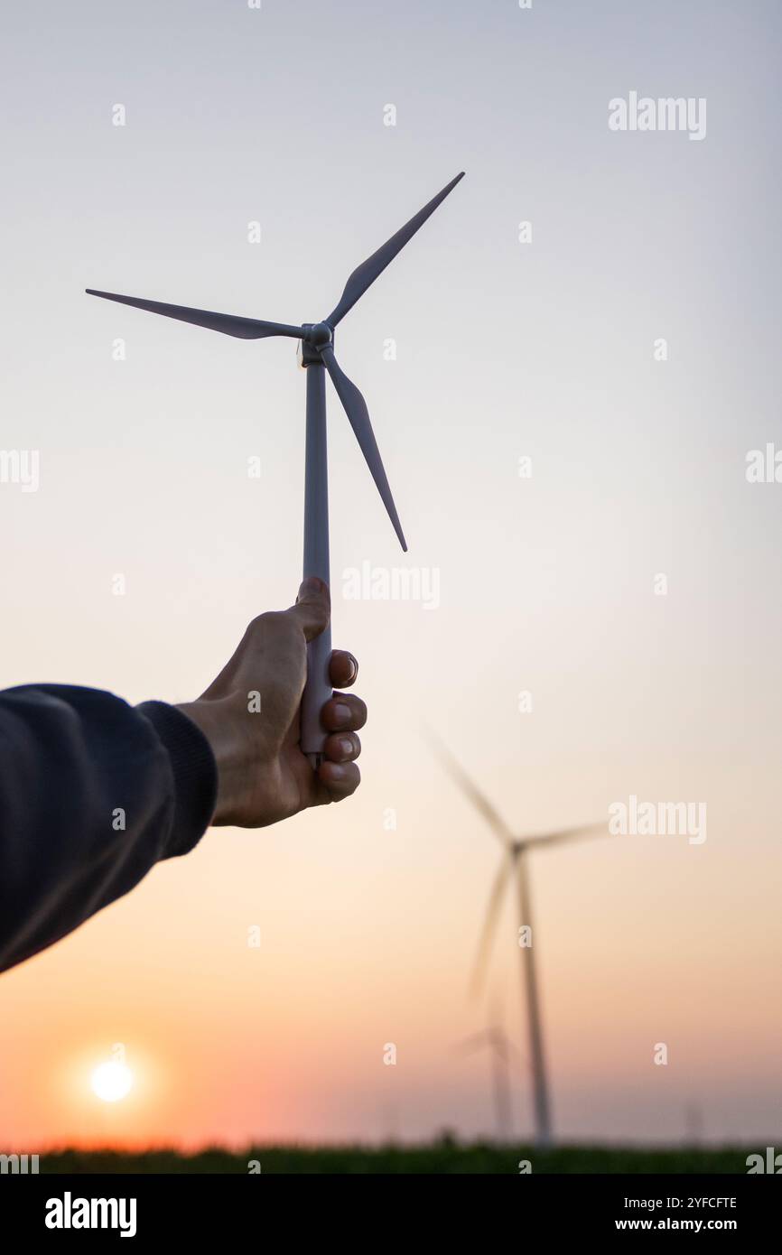 L'uomo tiene in mano la turbina eolica giocattolo. Turbine eoliche reali sullo sfondo. Foto Stock