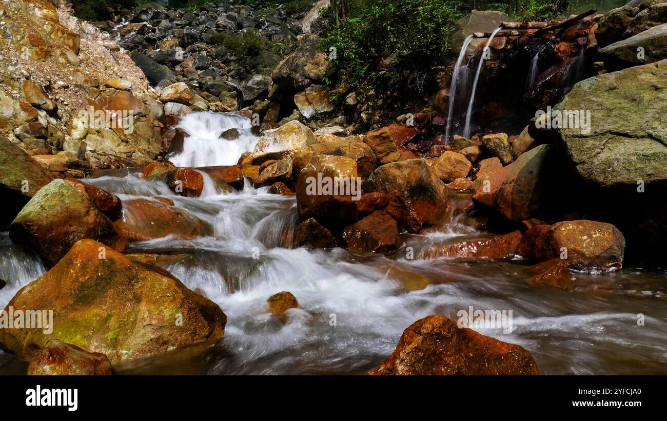 L'acqua calda che scorre dal bambù si fonde con il fiume di acqua fredda che proviene dalla cascata sopra di esso. Foto Stock
