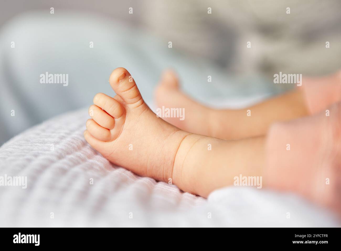 Primo piano dei piccoli piedini per neonato con abbigliamento rosa, comodamente appoggiati su una coperta leggera morbida. Foto Stock