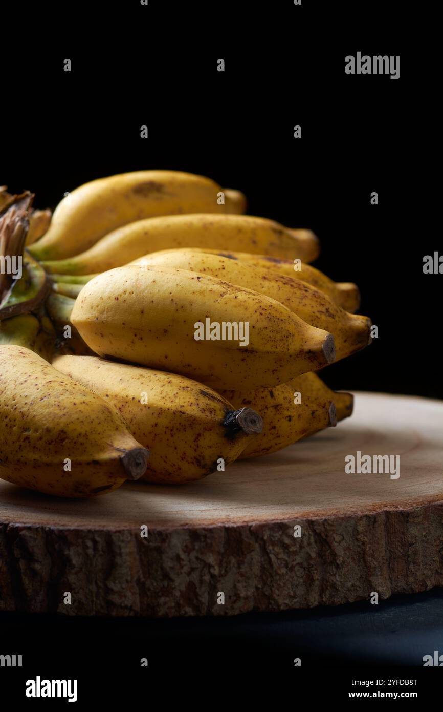 mazzo di banane fresche su vassoio di legno, frutta tropicale matura con pelle macchiata messa a fuoco morbida con sfondo scuro e morbido con spazio per copiare Foto Stock