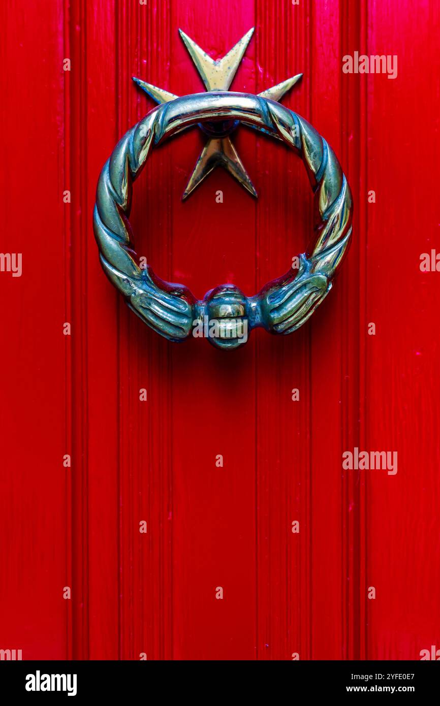 Primo piano di una porta decorativa in bronzo che bussa su una porta di legno rosso brillante, che trasmette un'atmosfera classica e accogliente. Presenta un design decorato con una stella m Foto Stock