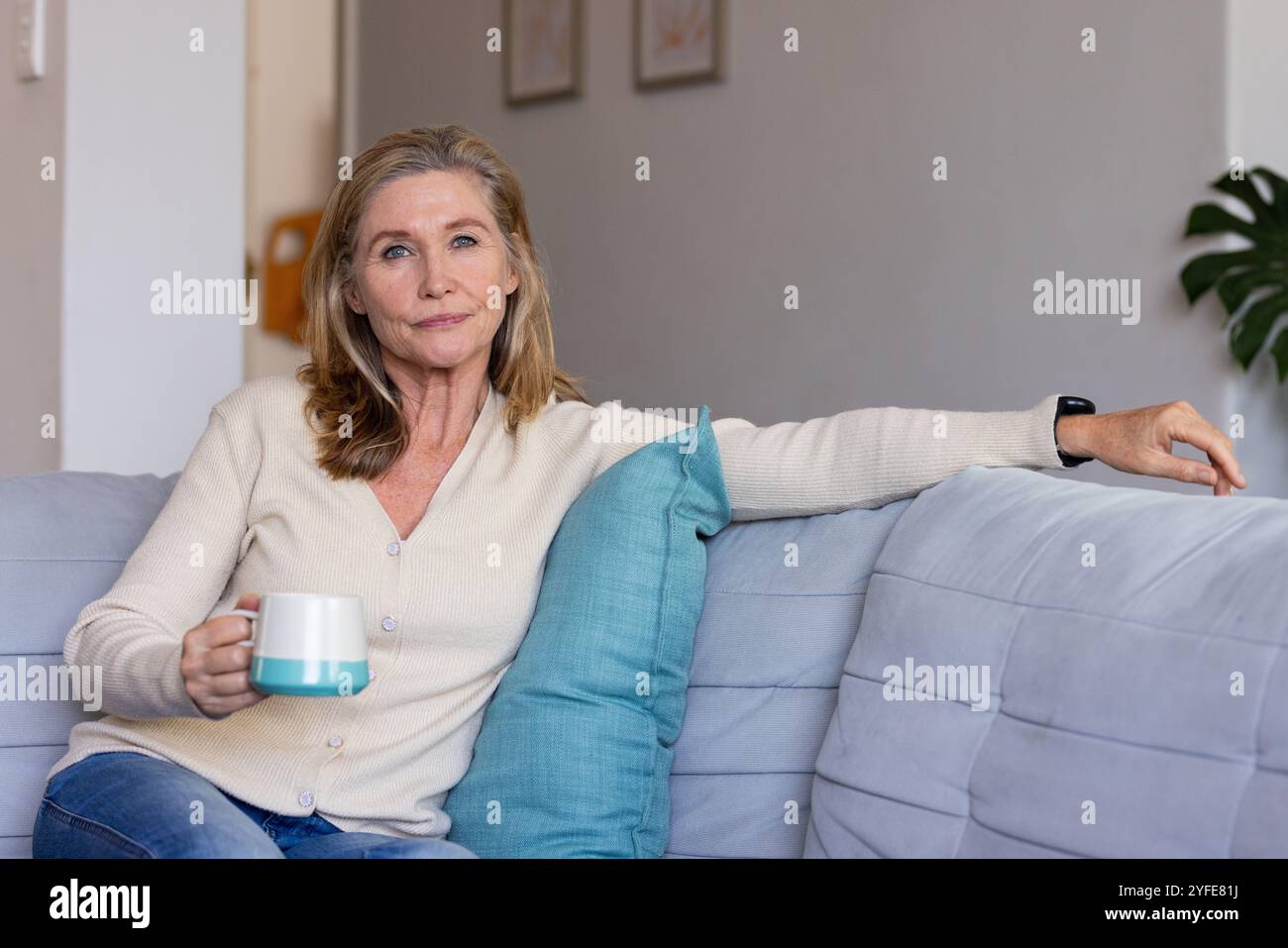 Rilassatevi a casa, una donna anziana che si gusta un caffè su un comodo divano Foto Stock