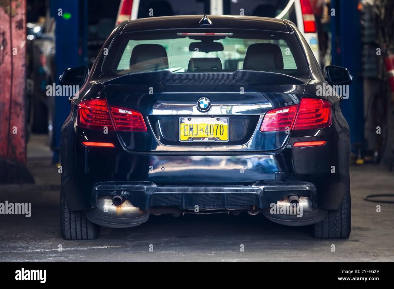 Vista posteriore di una BMW nera parcheggiata all'interno di un'officina di riparazione automobilistica con targhe New York. Foto Stock