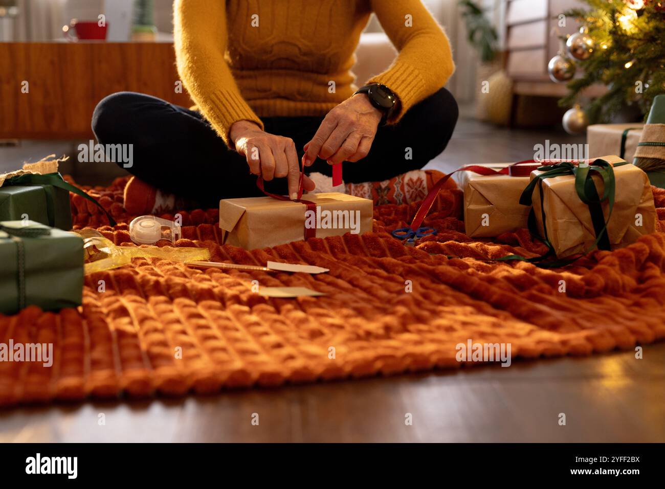 Avvolgere i regali di Natale su un'accogliente coperta vicino all'albero decorato a casa Foto Stock