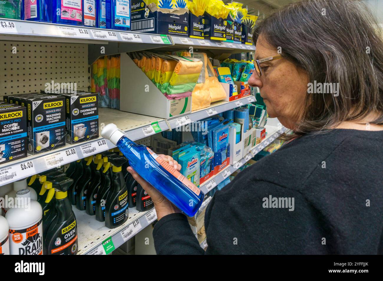 Donna che legge l'etichetta su una bottiglia di detergente e sgrassante. Foto Stock
