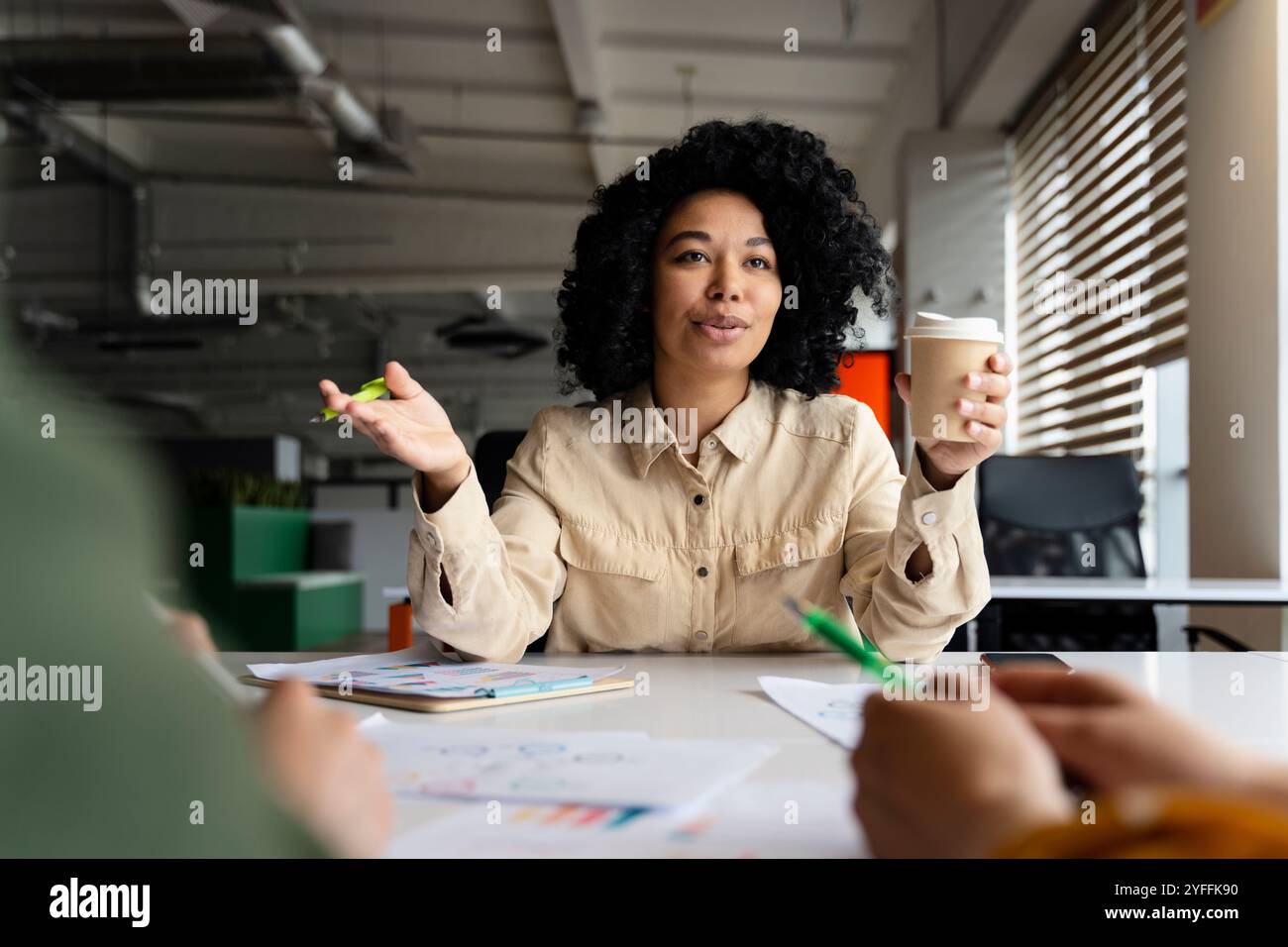 Manager Woman sta conducendo una riunione d'affari con il suo team, gestendo mentre tiene una tazza di caffè Foto Stock