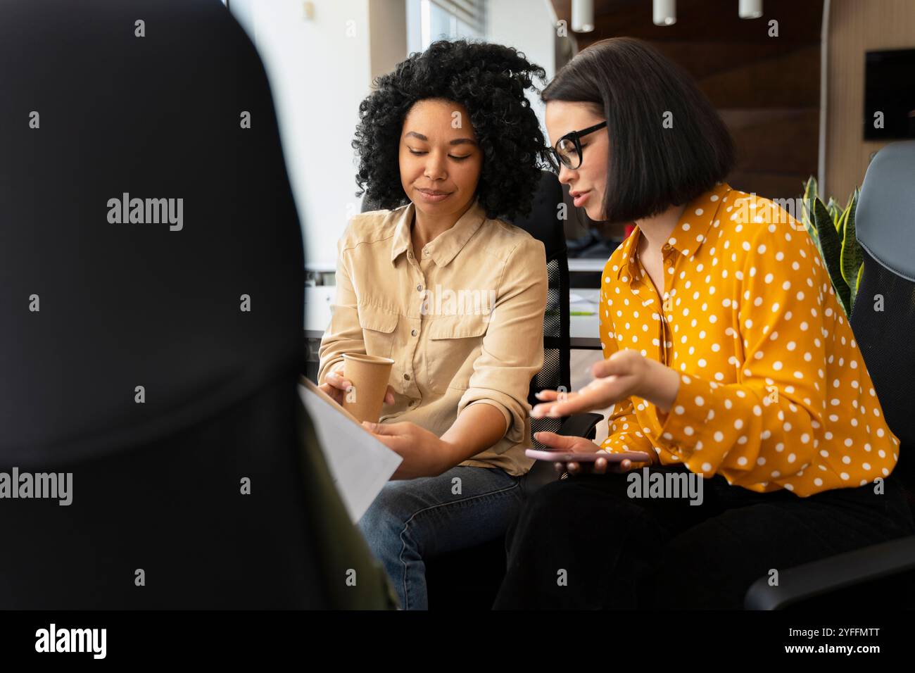 Due donne d'affari stanno avendo una riunione informale in un ufficio moderno, discutendo documenti e idee Foto Stock