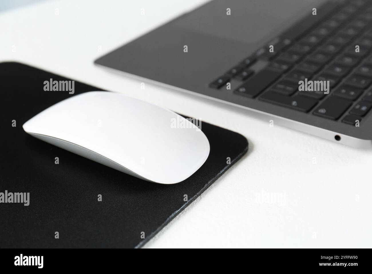 Mouse per computer con tappetino e laptop su tavolo bianco, primo piano Foto Stock