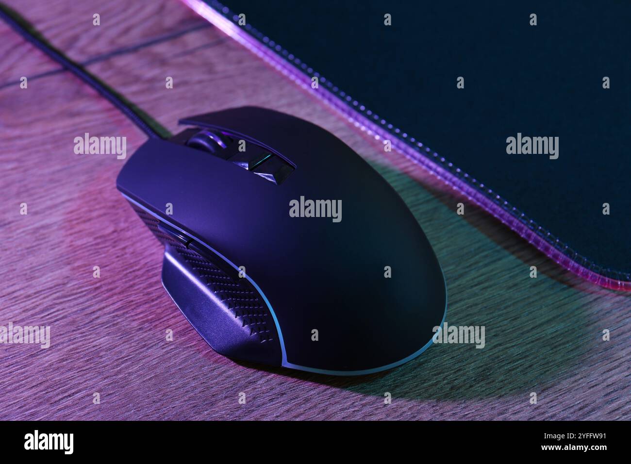 Mouse nero per computer e tappetino per mouse su un tavolo in legno con luci al neon, primo piano Foto Stock