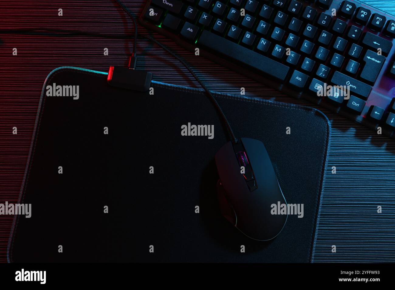 Mouse per computer, tappetino per mouse e tastiera su tavolo in legno scuro con luci al neon, posizione piatta Foto Stock