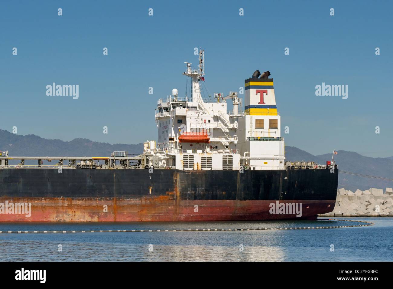 Manzanillo, Colima, Messico - 16 gennaio 2024: Petroliera nel porto di Manzanillo con un braccio galleggiante intorno ad esso per prevenire la fuoriuscita di petrolio Foto Stock