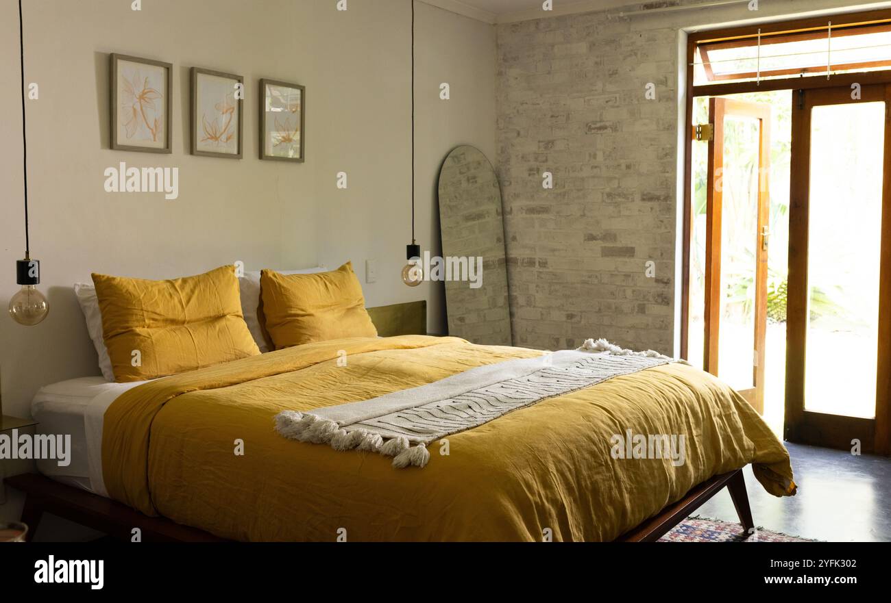 Accogliente camera da letto con biancheria da letto gialla e luce naturale da porte aperte, a casa Foto Stock