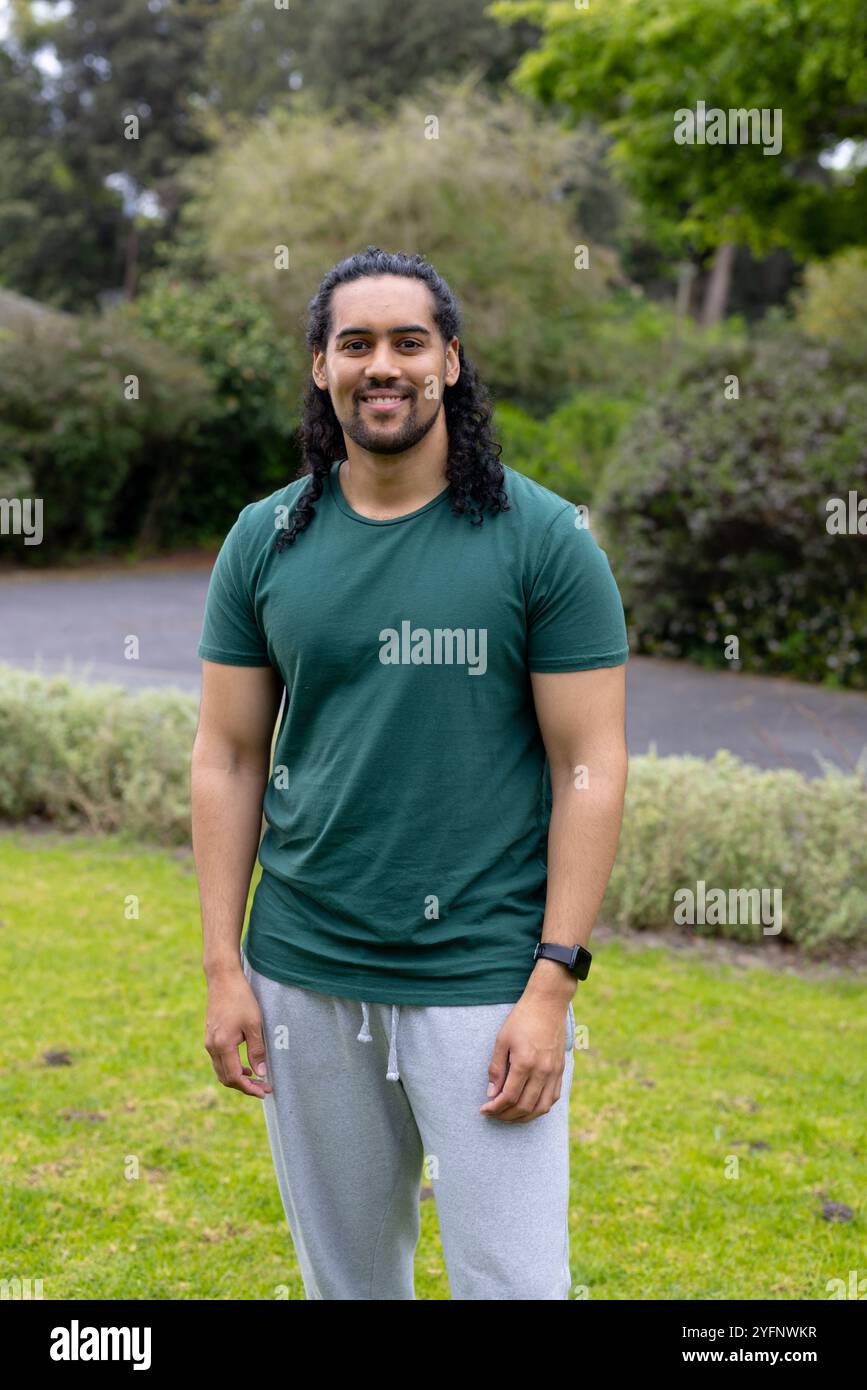 Un uomo sorridente in piedi nel parco indossa abiti informali, godendosi la vegetazione all'aperto Foto Stock