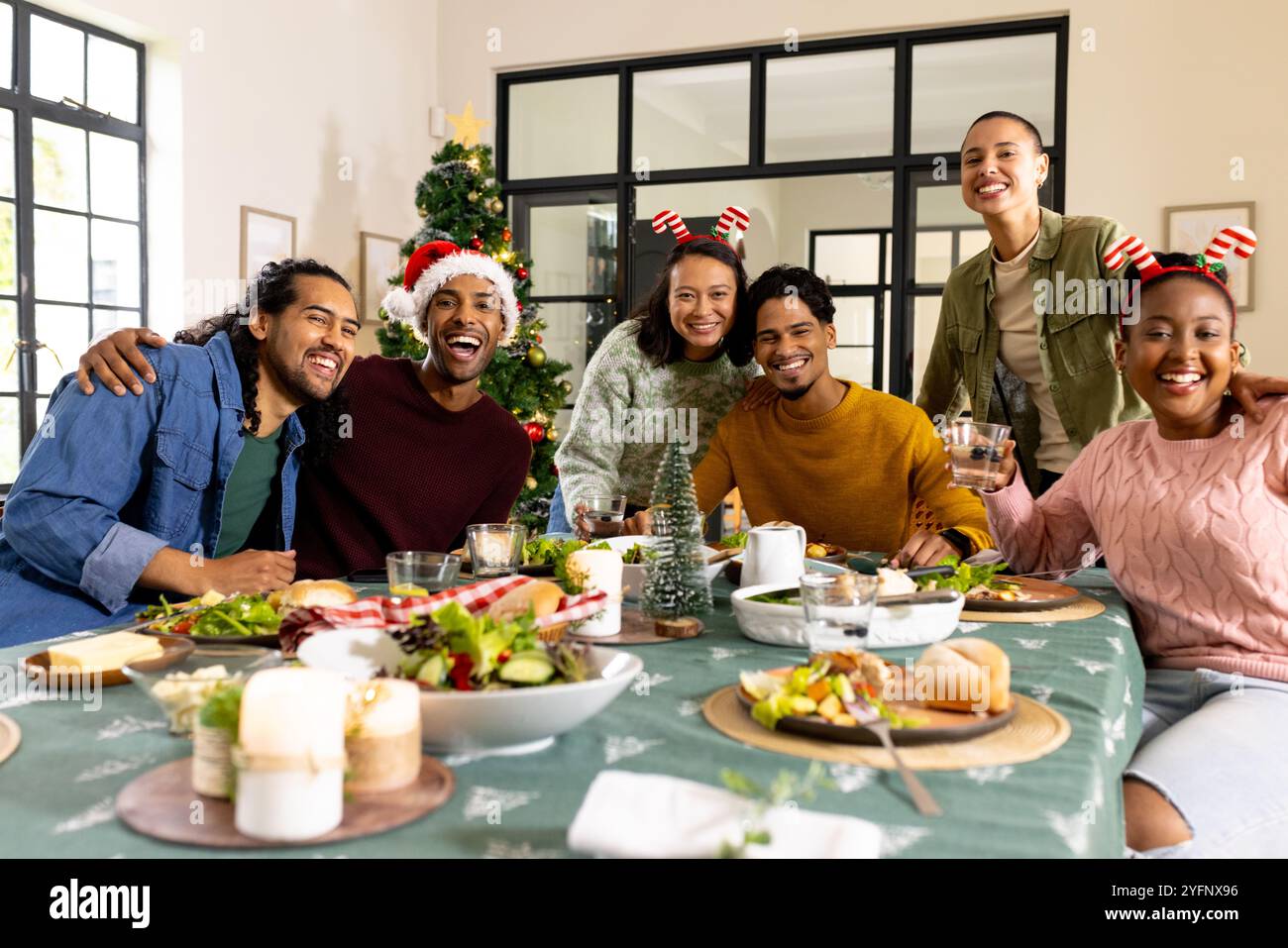 Amici multirazziali che festeggiano il Natale insieme, gustando un pasto festivo e festeggiando a casa Foto Stock