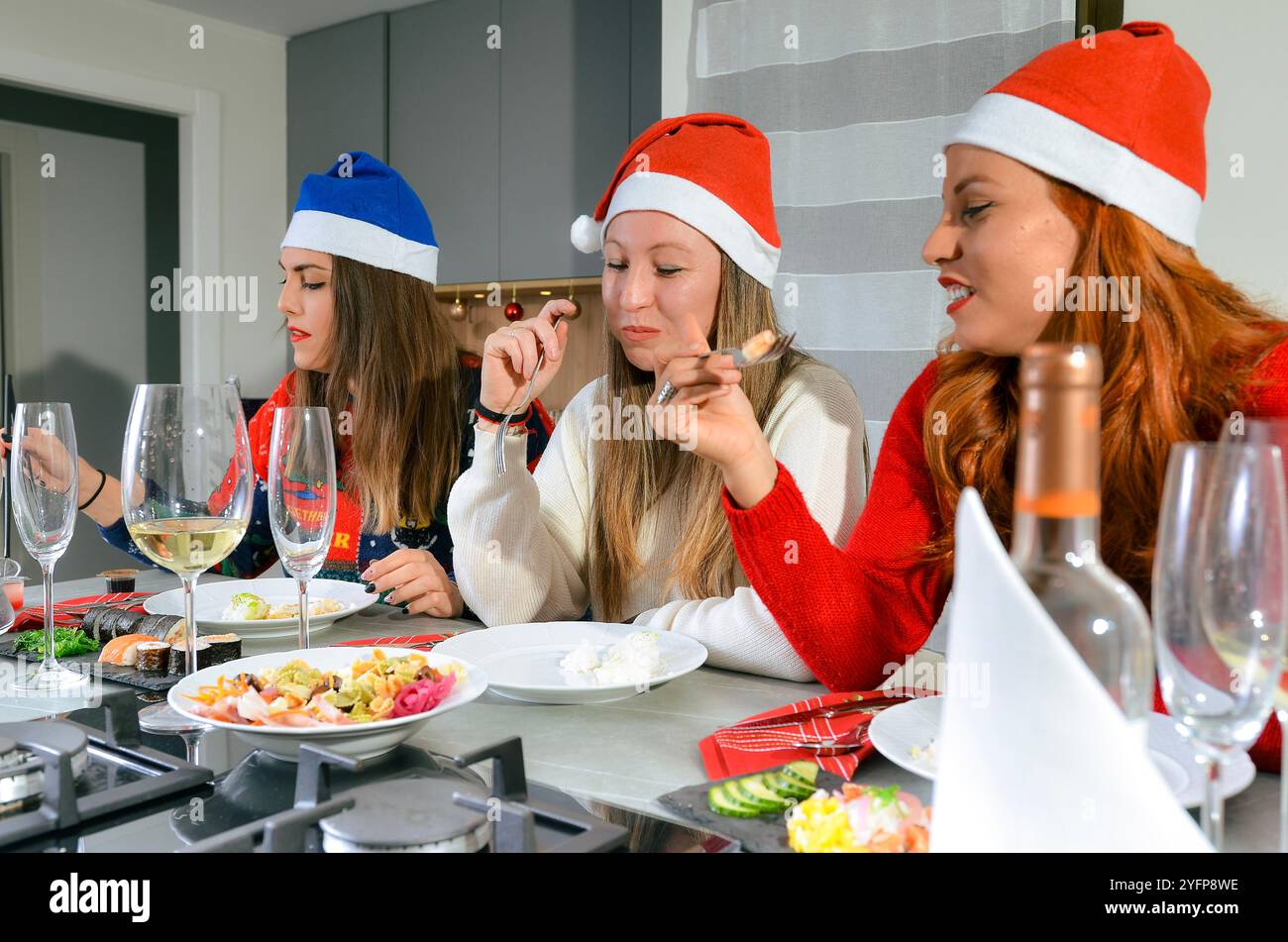 Tre donne che indossano cappelli di natale si godono la cena di natale con sushi e altri piatti Foto Stock
