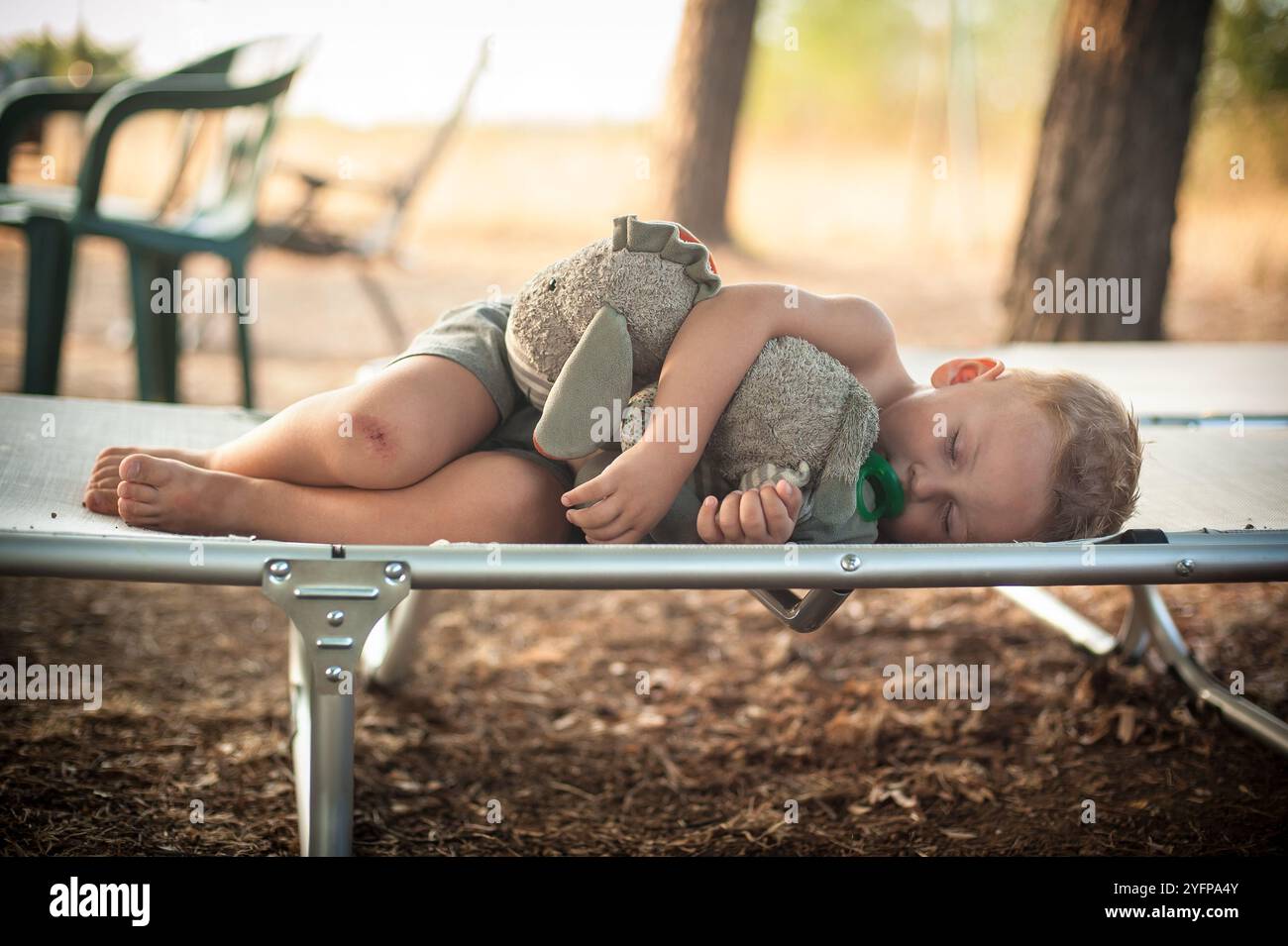 Un bambino sdraiato comodamente su una culla, tenendo vicino un animale imbottito mentre si gode un tranquillo pisolino in un tranquillo ambiente all'aperto. Il caldo pomeriggio Foto Stock