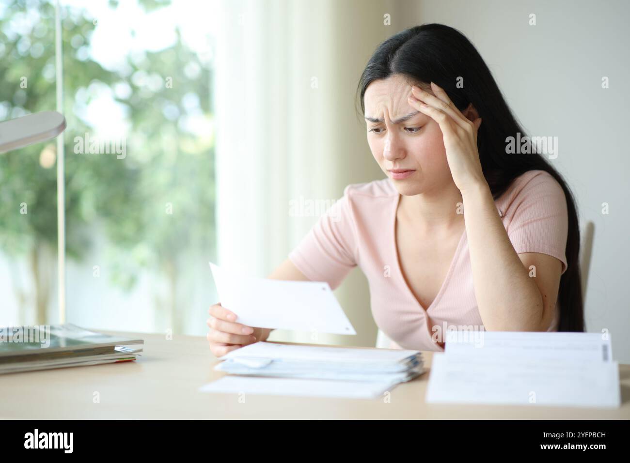 Preoccupata donna asiatica che si lamentava di controllare la fattura cartacea seduta a casa Foto Stock