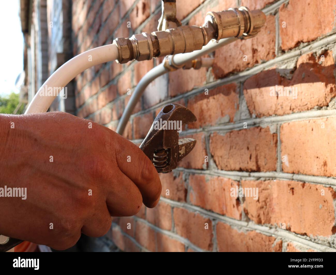 la mano porta la chiave a gas nel sistema di tubi in plastica sottili bianchi che escono da pareti in mattoni rossi all'aperto, ripara con l'attrezzo manuale di tubazioni su strada Foto Stock