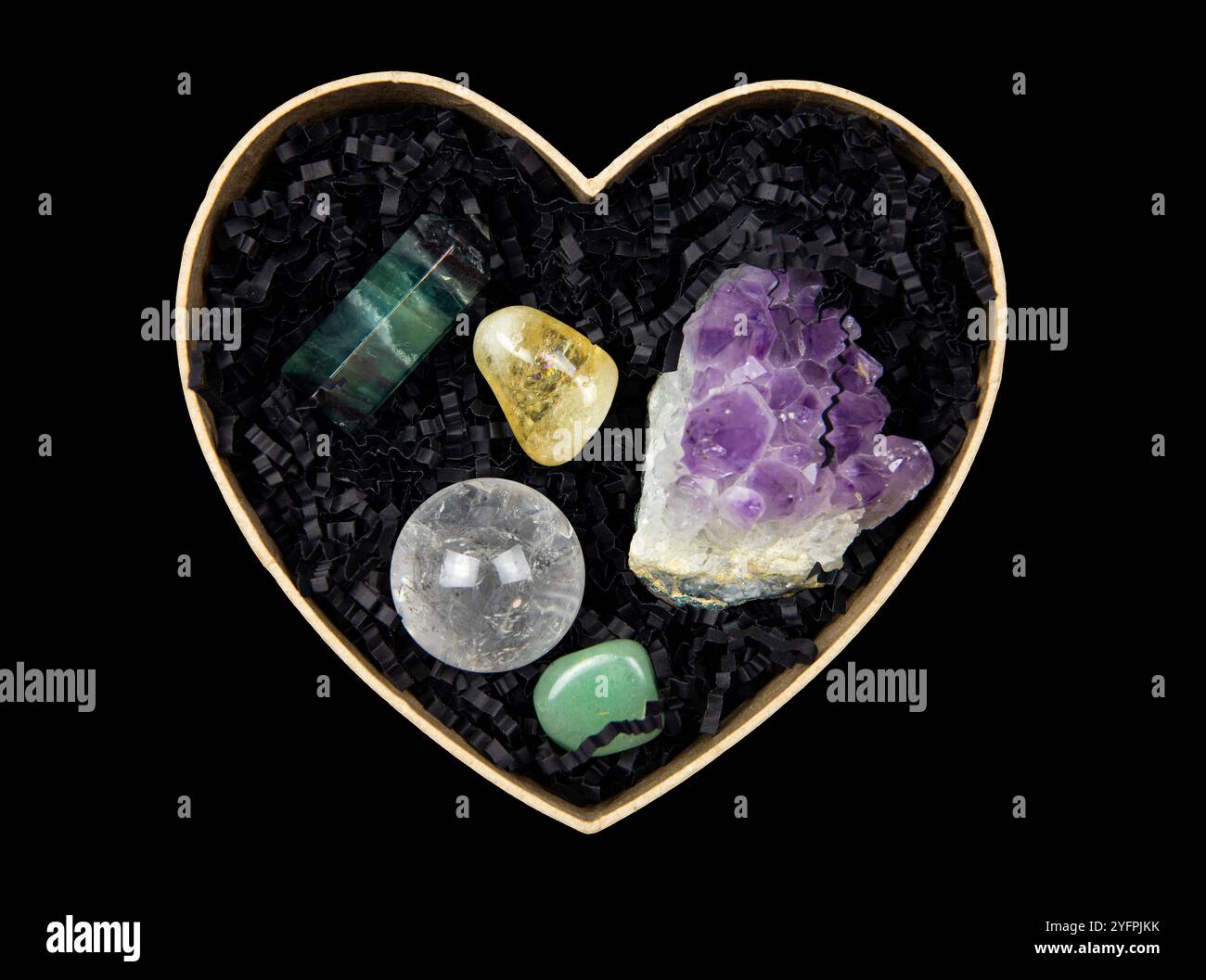 Vista dall'alto della scatola regalo a forma di cuore aperta con carta grattugiata di colore nero - riempitivo per scatole regalo e pietre semi-preziose all'interno. Foto Stock