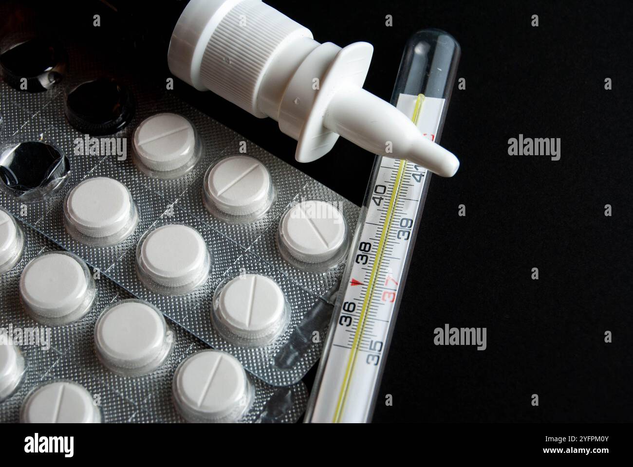 Una foto concettuale con pillole di paracetamolo, un termometro e uno spray nasale posto su uno sfondo nero, che simboleggia i rimedi per l'influenza stagionale. Foto Stock