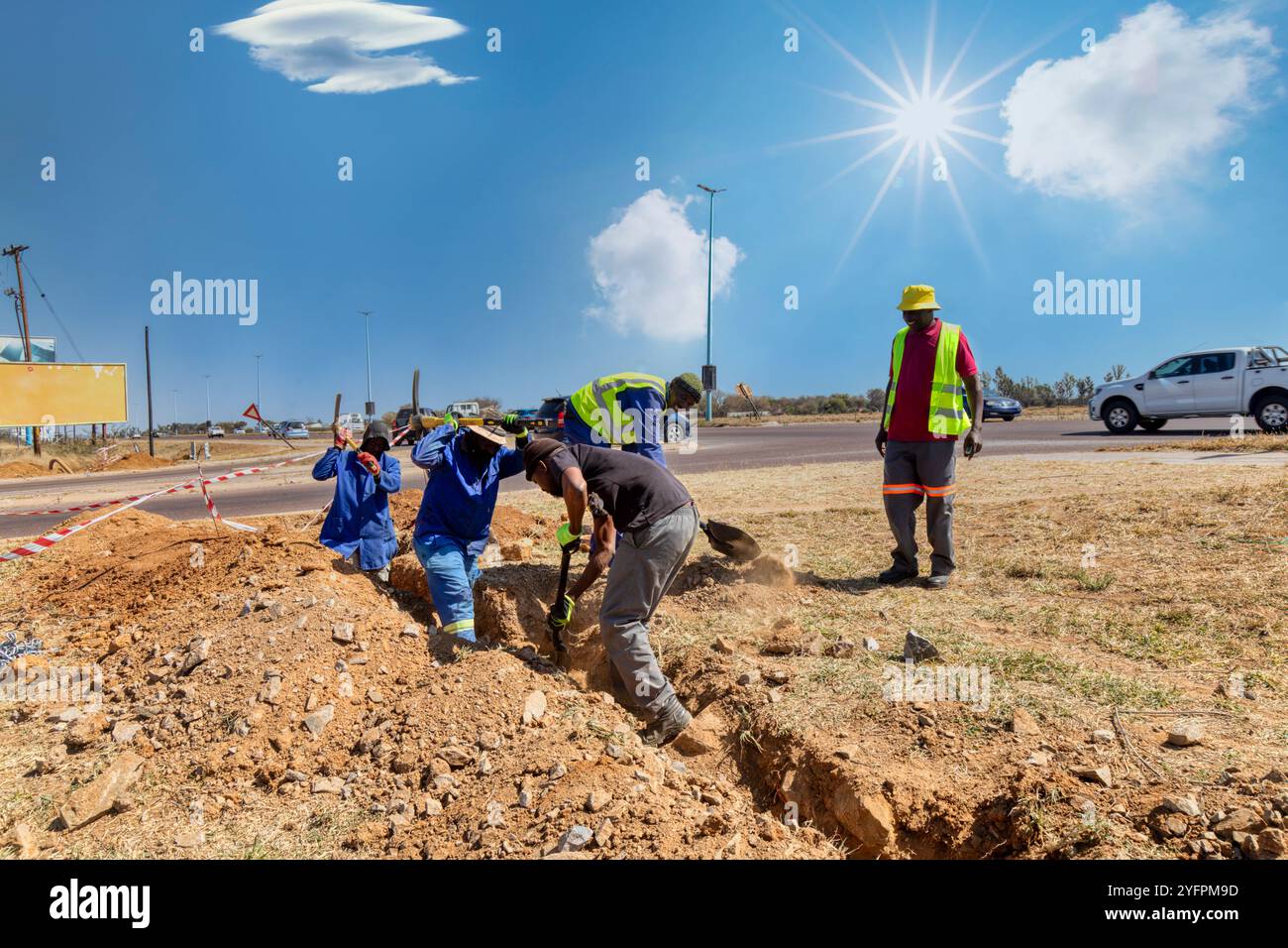 Gruppo di operai africani che scavano una trincea sul lato dell'autostrada installando fibre ottiche per l'azienda di telecomunicazioni Foto Stock