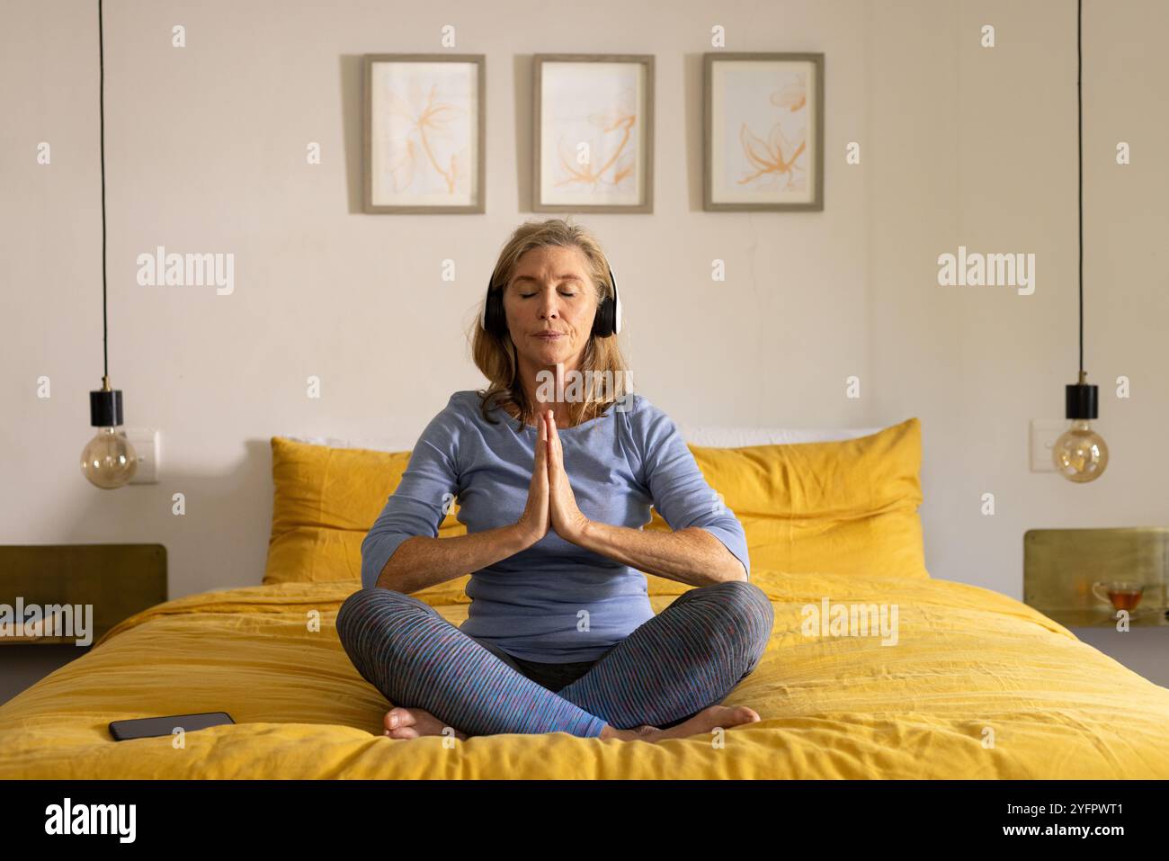 donna anziana che meditava sul letto con le cuffie, trovando pace a casa Foto Stock