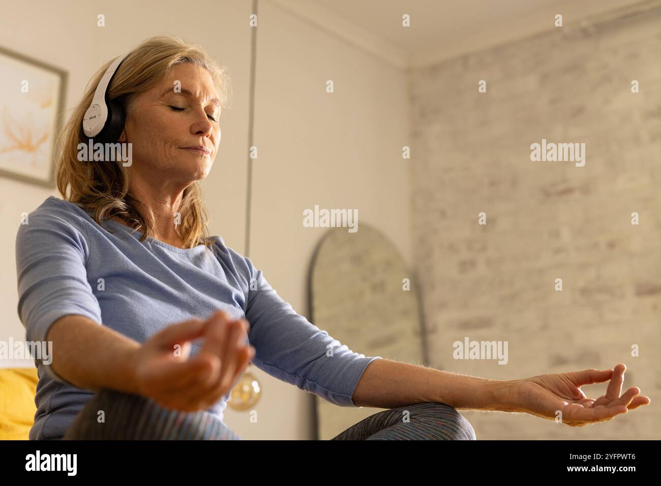 donna anziana che meditava con le cuffie a casa, trovando pace interiore Foto Stock